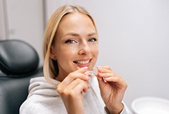 Closeup of woman smiling while holding clear aligner