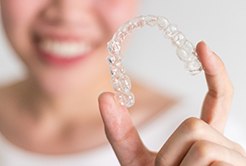 Smiling patient holding clear aligner